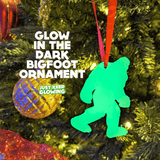 Glow-in-the-dark Bigfoot Christmas ornament hanging on a festive tree, emitting a bright green light.