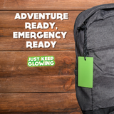 Glow Tag for Backpack - Adventure and Emergency Preparedness. 'Adventure Ready, Emergency Ready' message. Just Keep Glowing brand. Bright green glow tag attached to a gray backpack against a wooden background.  Essential for hiking, camping, and outdoor safety.  Long-lasting glow for visibility in the dark.  No batteries needed.