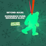 Close-up of the glowing Bigfoot ornament with text "BEYOND BULBS. EXPERIENCE PURE, REUSABLE GLOW." highlighting its rechargeable feature.