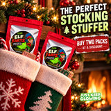 Two Elf Farts Christmas gift pouches tucked into red and green stockings beside a decorated fireplace, with a sign promoting a discounted two-pack stocking stuffer gift.