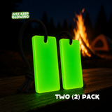 Two reusable glow in the dark bars for camping and emergency kits, glowing green beside a campfire with black carrying cords.