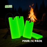 Four-pack of Forever Glow Bars, reusable glow in the dark camping lights with black paracord loops, glowing green beside a campfire.