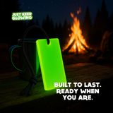 Durable, reusable Forever Glow Bar glowing green beside a camping mug and campfire, featuring a black paracord loop for easy carrying.