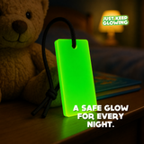 Forever Glow Bar reusable glow in the dark night light for kids, glowing green beside a teddy bear and bedside lamp.