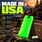 Forever Glow Bar glowing green on wet rocks beside a backpack and American flag, highlighting waterproof construction, reusable design, and Made in USA emergency gear.