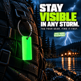 Waterproof Forever Glow Tag with stainless steel cable loop attached to a black emergency backpack in a storm, showing a reusable green glow marker for locating gear in darkness.